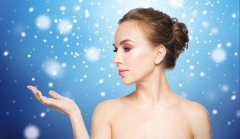 beauty, people, advertisement, winter and health concept - young woman holding something on palm of her hand over blue background and snow