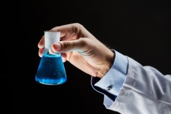 science, chemistry, research and people concept - close up of scientist hand holding test flask with chemical over black background