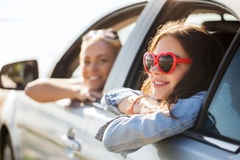 summer holidays, valentines day, travel, road trip and people concept - happy teenage girls or young women heart shaped sunglasses in car at seaside