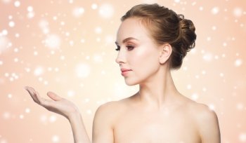 beauty, people, advertisement, winter and health concept - smiling young woman holding something on palm of her hand over beige background and snow