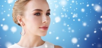 jewelry, luxury, christmas, holidays and people concept - close up of smiling woman in white dress wearing pearl earring over blue background and snow
