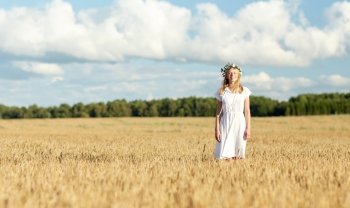 happiness, nature, summer holidays, vacation and people concept - happy smiling young woman or teenage girl in wreath of flowers and white dress on cereal field