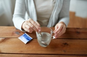 healthcare, medicine and people concept - close up of woman stirring medication in cup with spoon