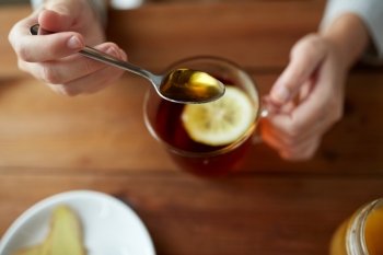 healthy food, eating and ethnoscience concept - close up of woman adding honey to tea cup with lemon