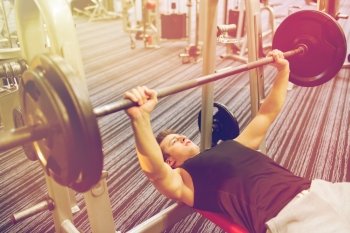 sport, bodybuilding, lifestyle and people concept - young man with barbell flexing muscles and making bench press in gym