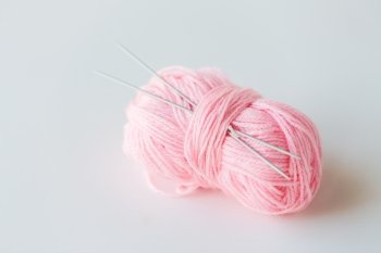 handicraft and needlework concept - knitting needles and ball of pink yarn on white. knitting needles and ball of pink yarn