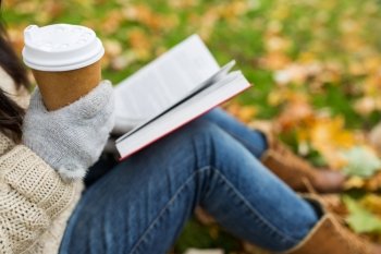 season, technology and people concept - close up of young woman reading book and drinking coffee from paper cup in autumn park