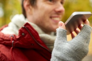 leisure, technology, communication and people concept - close up of smiling hipster man using voice command recorder or calling on smartphone in autumn