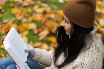 season, education, literature and people concept - close up of woman reading book in autumn park