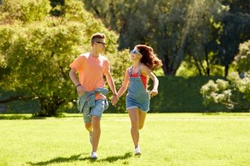 holidays, vacation, love and people concept - happy smiling teenage couple holding hands and running at summer park