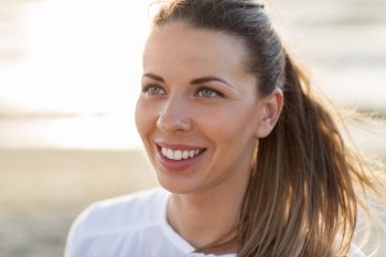 people, facial expression and emotion concept - happy young woman face on beach