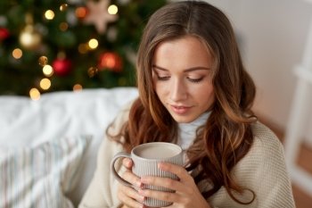 christmas, holidays and people concept - happy young woman with cup of coffee or cocoa drink at home