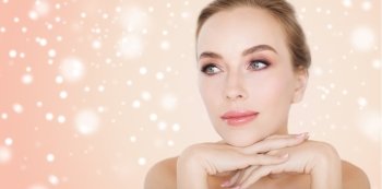 beauty, people, winter and bodycare concept - close up of beautiful young woman face and hands over beige background and snow