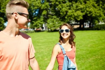 holidays, vacation, love and people concept - happy smiling teenage couple walking and looking at each other in summer park