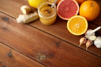 traditional medicine, cooking, food and ethnoscience concept - honey, citrus fruits with ginger and garlic on wooden background