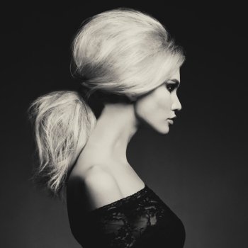 Black and white fashion studio portrait of beautiful blonde woman with elegant hairstyle on black background