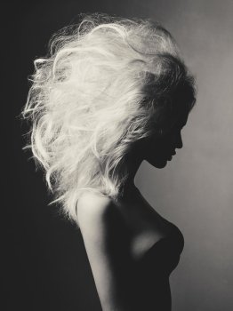 Black and white fashion studio portrait of beautiful blonde woman with volume hairstyle on black background