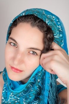 Young female model with black hair and a blue open shoulder summer dress, wearing a blue shawl over her hair.