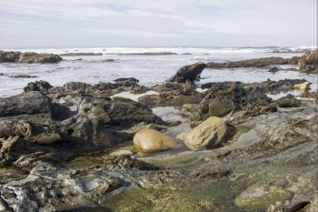 Two big boulders lie in the water of a rock pool on a rugged coastline.