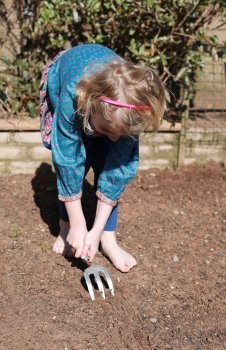 Pretty blonde haired girl making rows in the soil to plant with seeds