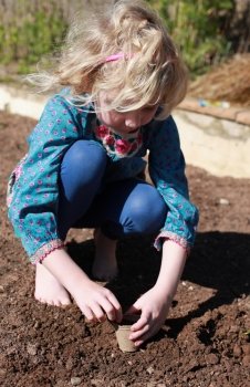Pretty blonde haired girl planting a seed in a pot