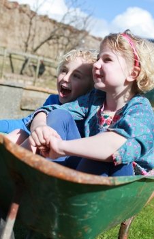 Brother and sister sitting in a wheel barrow having fun