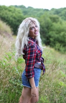 Beautiful healthy young woman outdoors wearing casual outfit of denim shorts and a checked shirt.