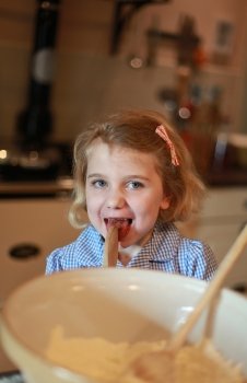 A young girl who has been baking is liking the spoon.
