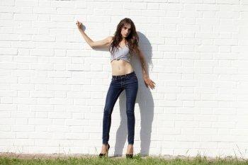 Beautiful sexy young brunette in blue jeans on white brick wall