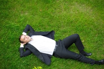 Happy Young businessman in a suit lying on the green grass, view from above