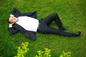 Happy Young businessman in a suit lying on the green grass, view from above