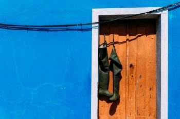 Pair of wellies boots hanging from brown rustic doorway with bright blue wall facade copy space.. Pair of wellies hanging from brown rustic doorway with bright blue wall facade copy space