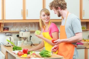 Happy young couple cooking. Woman and man having fun in modern kitchen indoor at home while preparing fresh vegetables food salad