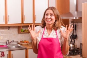 Frightened and worried woman wearing pink apron. Unhappy anxious and stressed housewife in kitchen. Negative facial emotion.. Unhappy housewife in kitchen