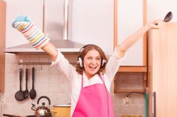Cooking preparing and making food concept. Modern beauty woman housewife cook chef wearing pink apron and listening music on earphones standing in kitchen.. Housewife cook in kitchen