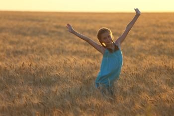 young girl joys on the wheat field  at the sunset time

