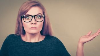 Nerdy woman in big eyeglasses having confused face expression pointing with palm open hand. Nerdy woman in eyeglasses being confused