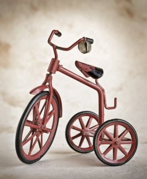 tiny red toy vintage metal tricycle, with rubber tires, small bell on the handelbars 