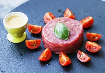 Tartare raw meat over black stone plate with tomatoes and egg cream, horizontal image