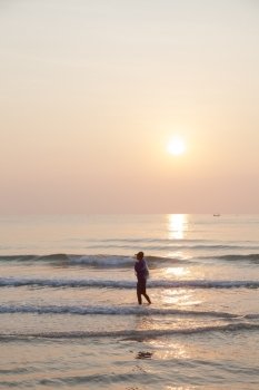Man walking on the beach. In the morning the sun rises over the ocean.