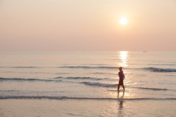 Man walking on the beach. In the morning the sun rises over the ocean.