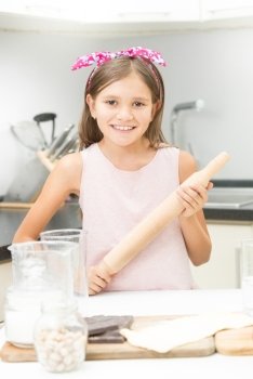 Cute girl with pink bow on hair posing with wooden rolling pin