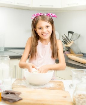 Beautiful smiling girl making dough for pie in white bowl