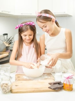 Two smiling girl making dough in white bowl on kitchen