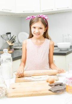 Cute smiling girl rolling dough on messy kitchen