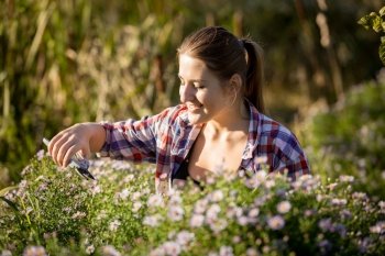Beautiful young woman pruning flowers with garden scissors