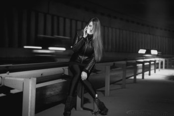 Black and white photo of young stylish woman talking by phone at night highway