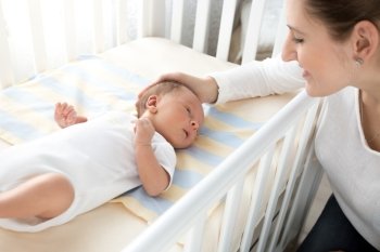 Portrait of happy smiling mother caressing her baby lying in cot