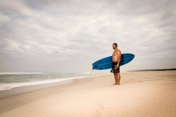 Surfer wathing the waves on the beach with his surfboard.