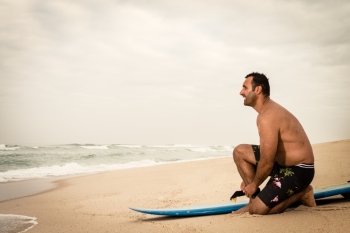 Surfer tying his surfboard’s leach on the beach.